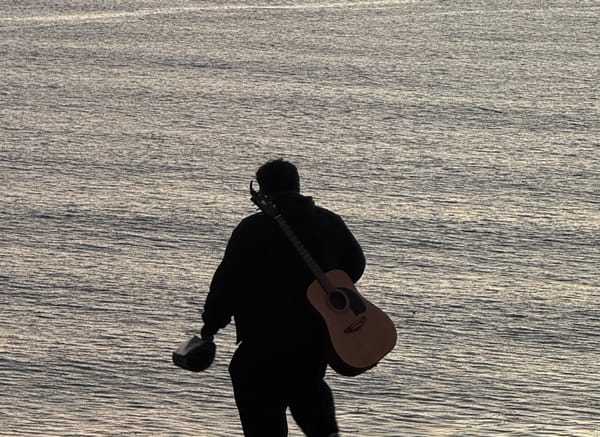 A man and his guitar form a silhouette against the ocean